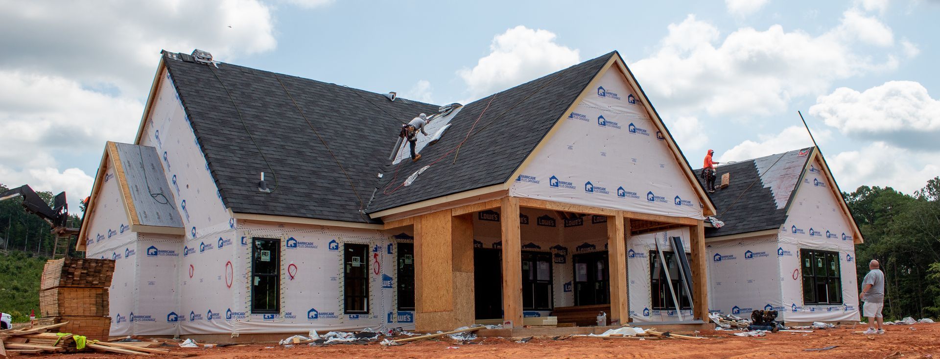House under construction, with roof and siding partially complete. Construction workers visible.