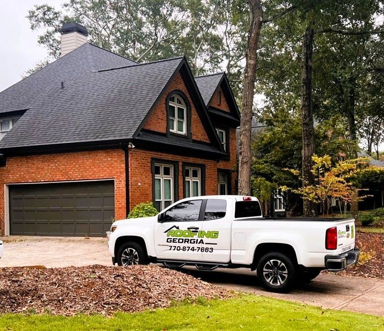 White truck parked in front of a brick house with a newly shingled roof.
