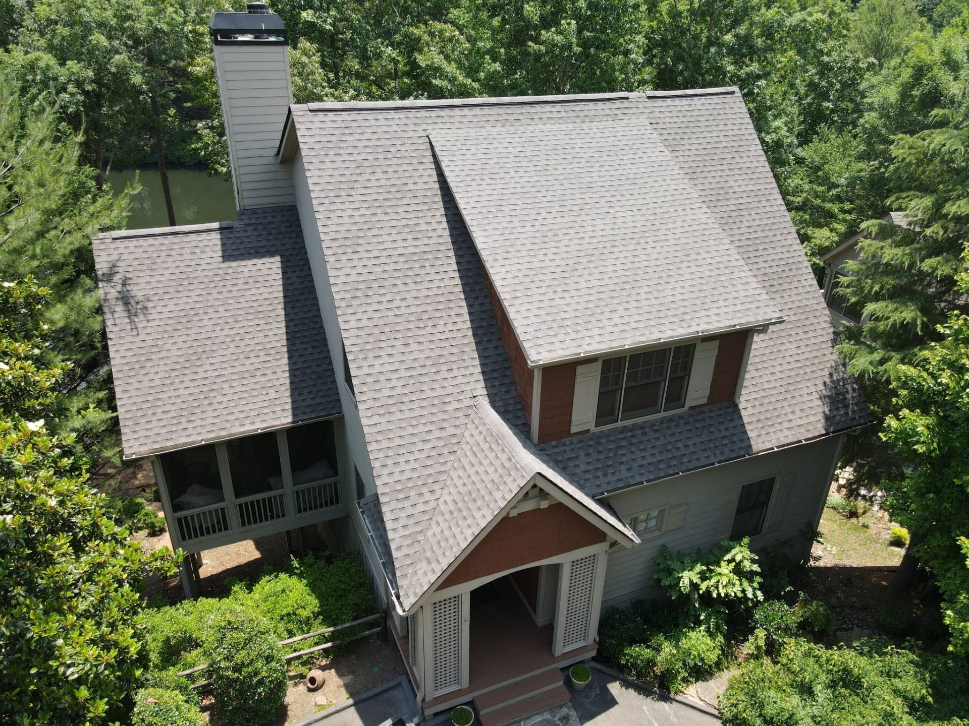 House with gray roof surrounded by trees. Red shutters and chimney. Porch with patterned screens.