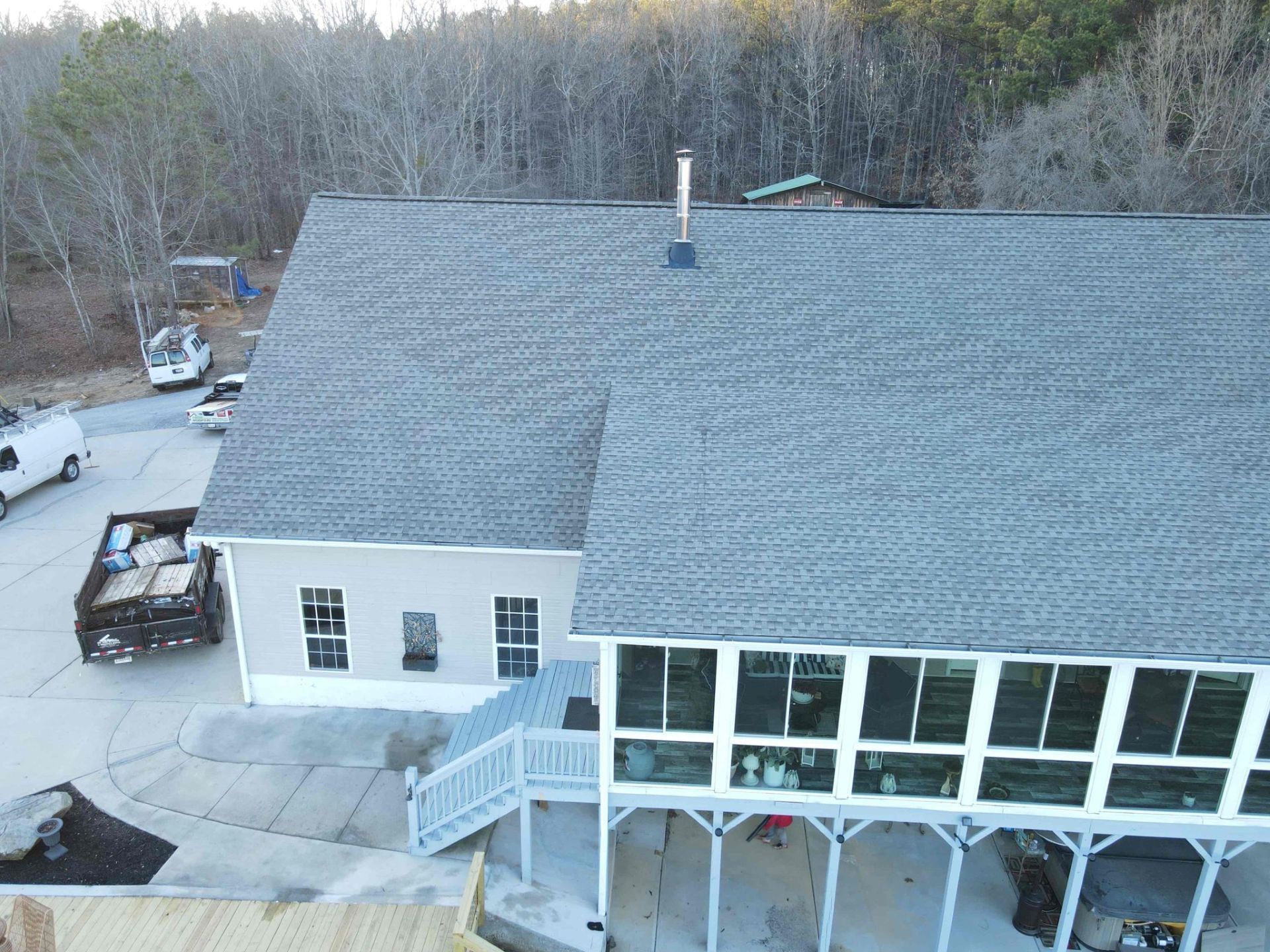 Gray roof of a building with a white porch and trees in the background. A dump truck and van are nearby.