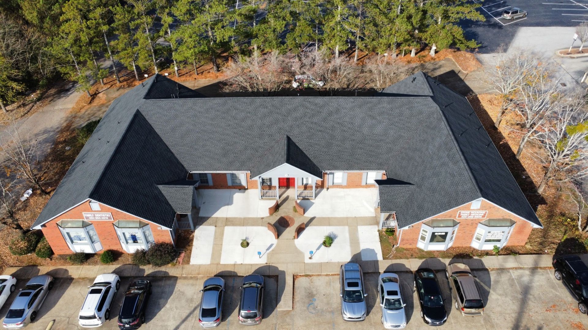 Aerial view of a one-story brick building with a dark roof. Cars are parked in front.