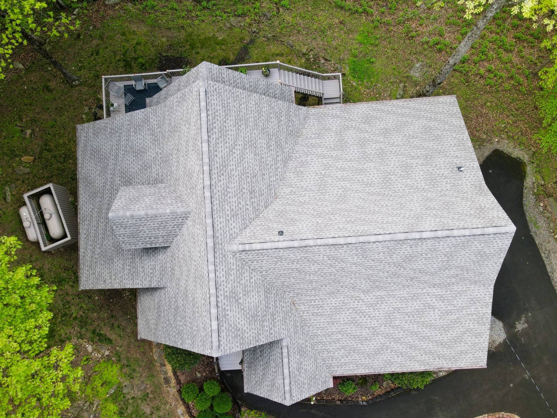 Overhead view of a house with a gray roof, surrounded by green trees and a driveway.