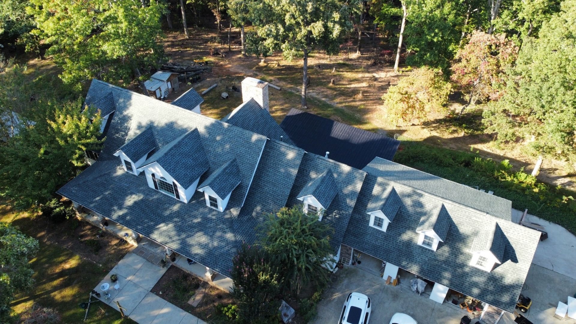 Aerial view of a large house with a gray roof and white trim surrounded by trees on a sunny day.