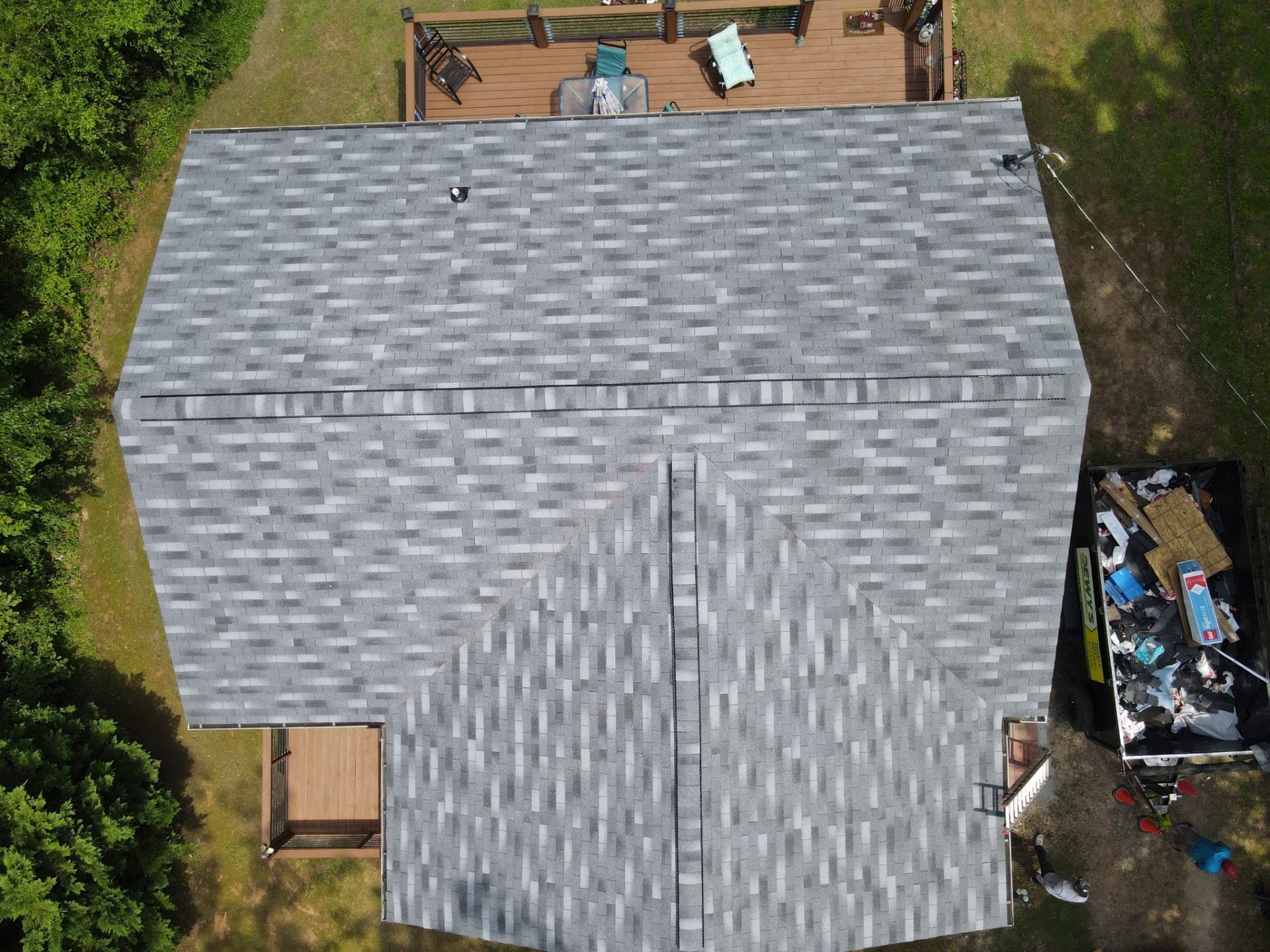 Aerial view of a gray shingle roof on a house with a wooden deck and surrounding greenery.