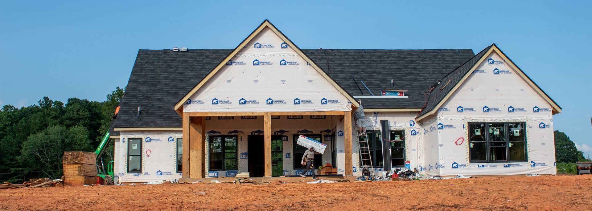 A house under construction, wrapped in white material, with a blue sky background.