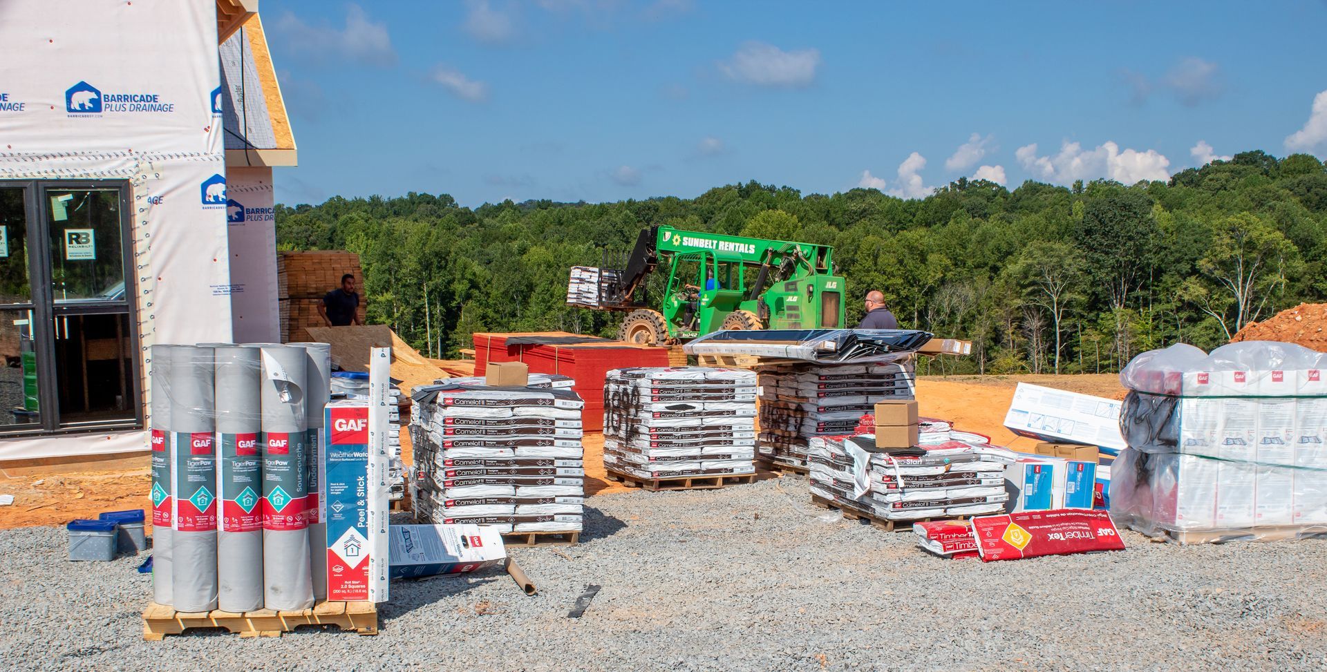 Construction site with stacks of building materials and a green forklift under a blue sky.