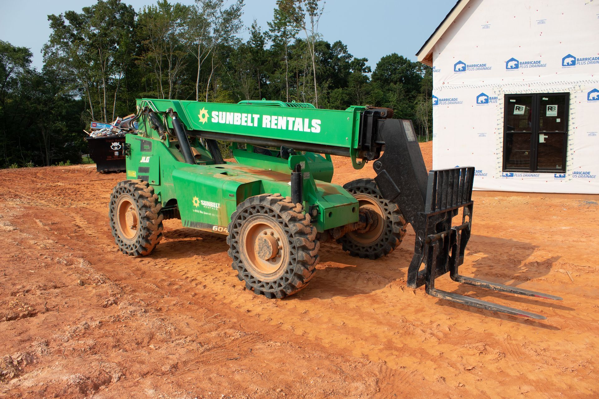 Green telehandler on a construction site with forks extended.