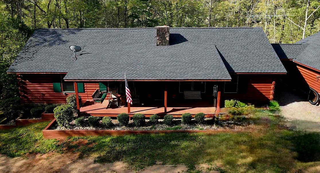 Red cabin with a porch and American flag, set in a wooded area.
