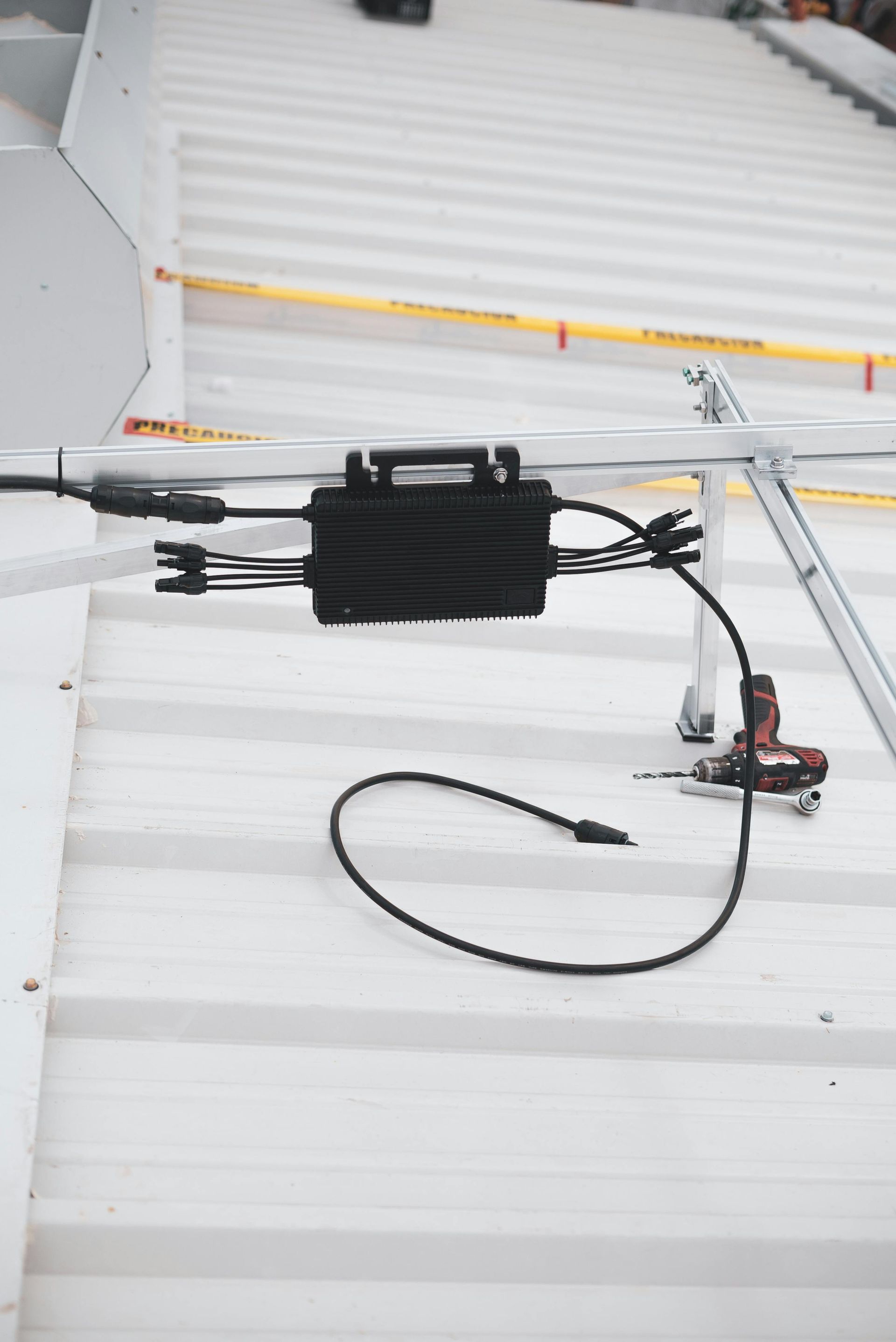Solar panel junction box installed on a corrugated metal roof. Black box with connected wires and tools.