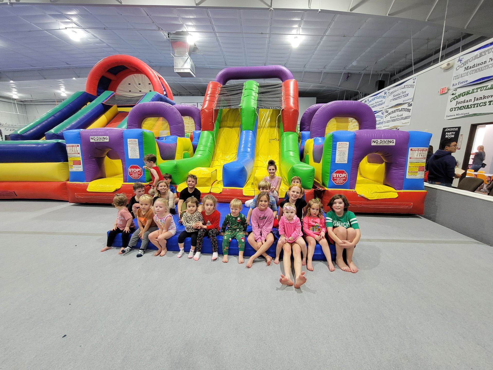 Children sitting in front of a colorful inflatable obstacle course in a gymnasium.