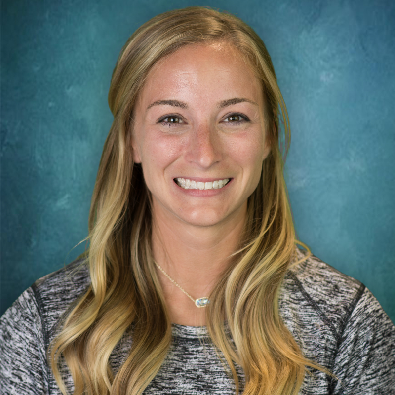 Blonde woman smiles, wearing a gray shirt, against a teal and blue gradient background.