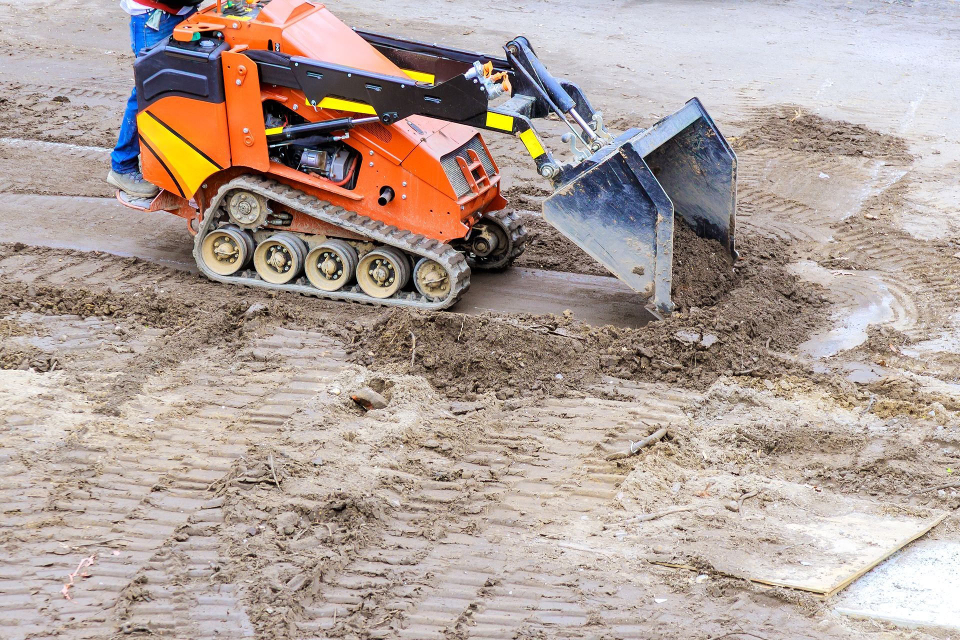 Orange and black mini-excavator with tracks scooping up dirt on a construction site.