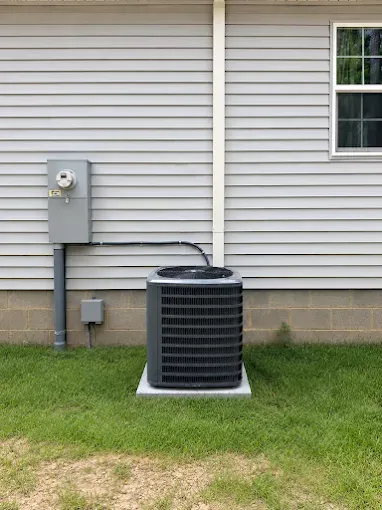 Outdoor air conditioner unit beside a house with siding and electrical meter box