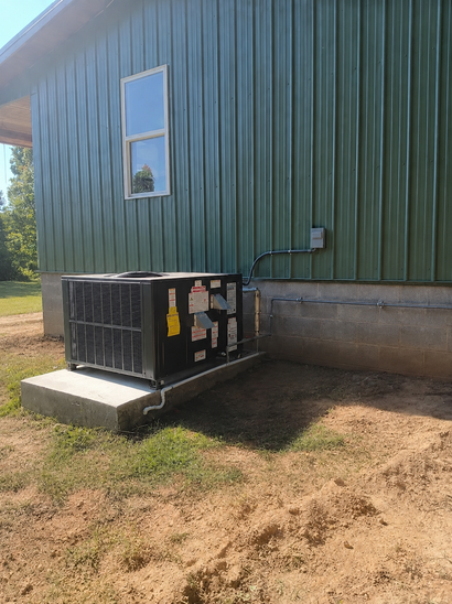 Outdoor HVAC unit beside a green metal building with a window and dirt ground