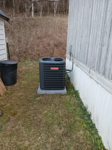 Outdoor air conditioner unit beside a white house, with a trash can nearby in a grassy yard.
