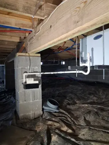 Crawlspace under a wooden floor with exposed pipes, white utility box, and plastic moisture barrier
