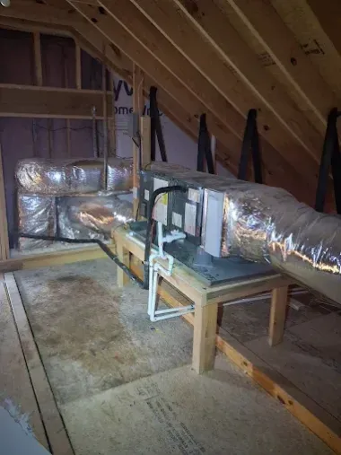 Attic with exposed rafters and insulated HVAC ductwork on a wooden support frame