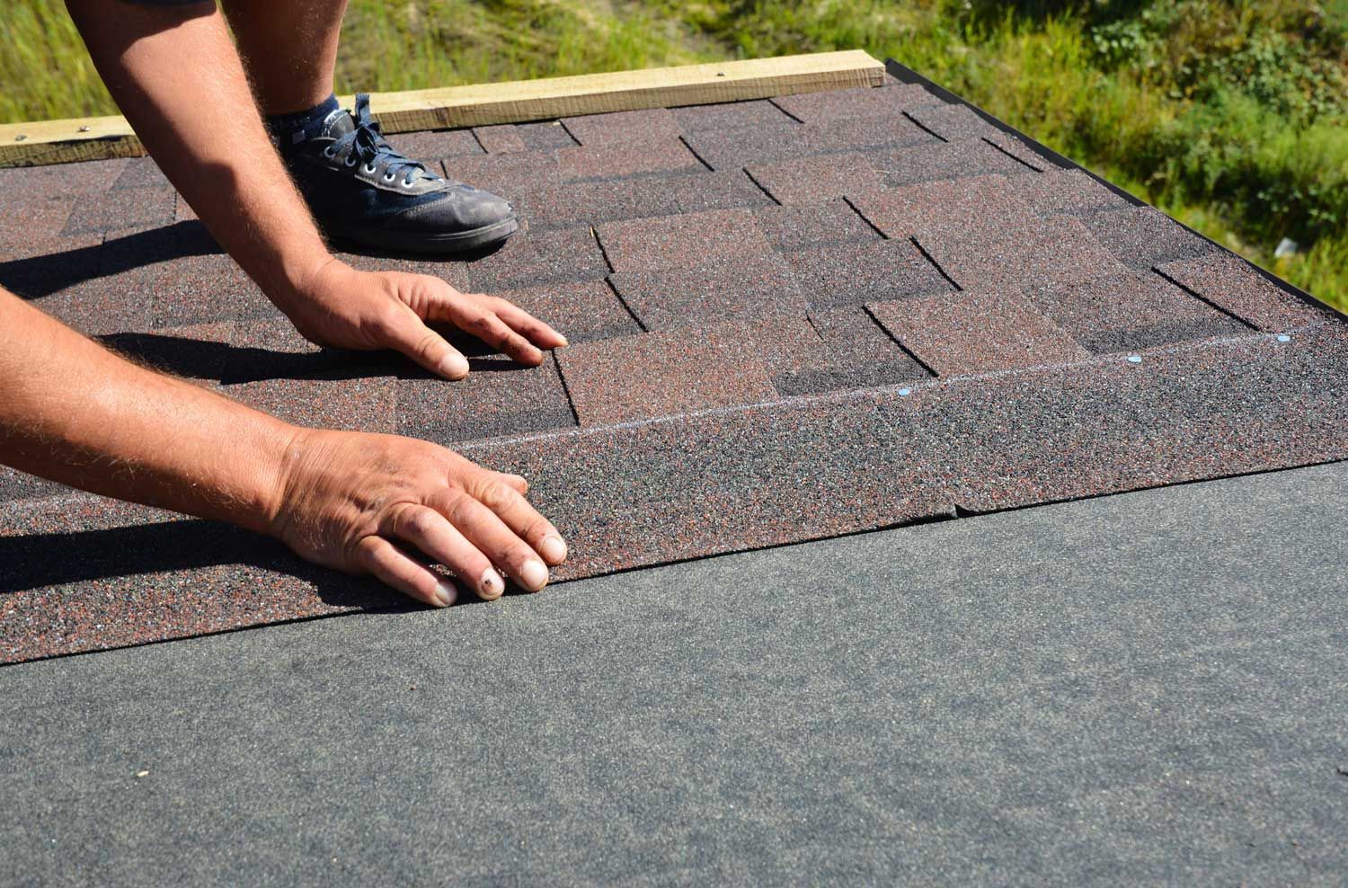 Roofer installing asphalt shingles on residential roof during roof repair and replacement project.