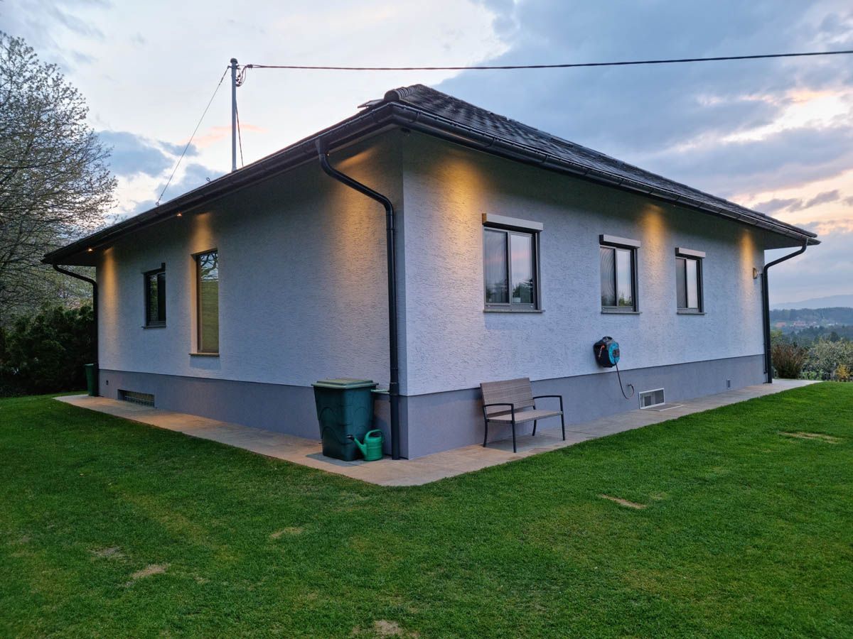Graues Haus mit schwarzen Zierleisten, Fenstern und Dach, umgeben von grünem Rasen.