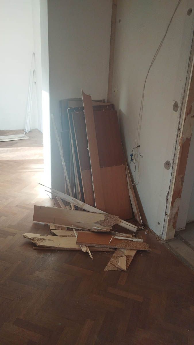 Haufen Bauschutt in einem Raum mit Hartholzböden, darunter Holzpaneele und eine beschädigte Tür.