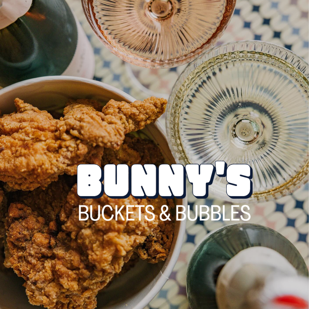 Champagne and fried chicken on a table. Bunny's Buckets & Bubbles logo on top of image