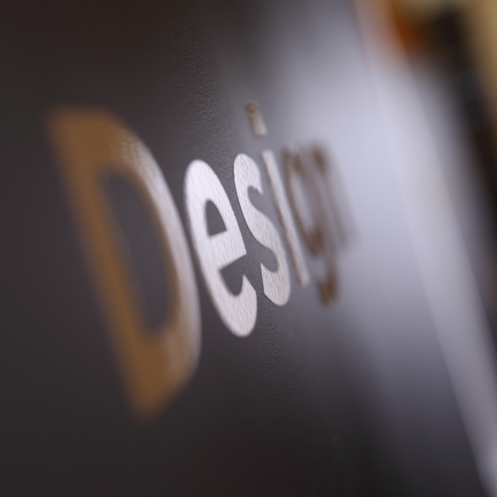 Blurred close-up of the word “Design” in white and gold on a dark surface.