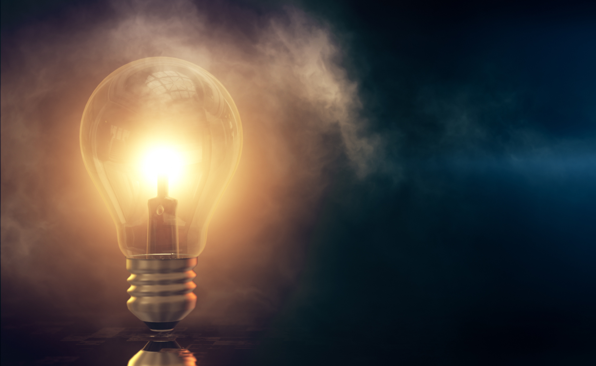 Glowing light bulb with a warm yellow light against a dark, smoky background
