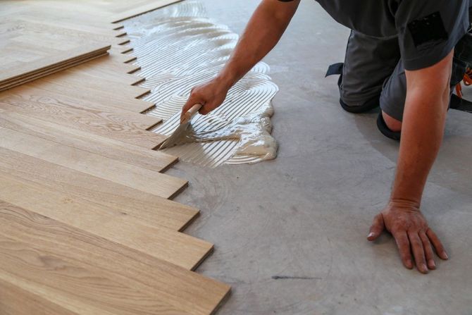 Person spreading adhesive on a floor while installing interlocking wood flooring tiles