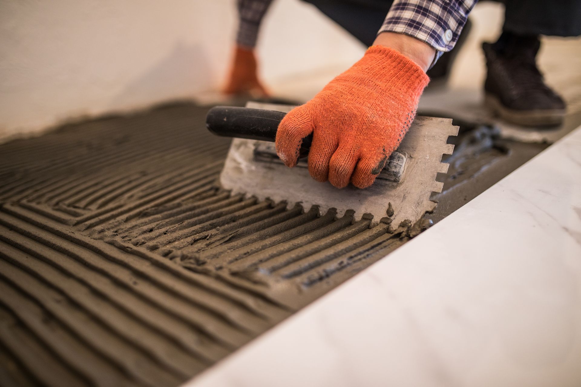 Orange-gloved hand spreading mortar with a trowel on a tiled floor under construction