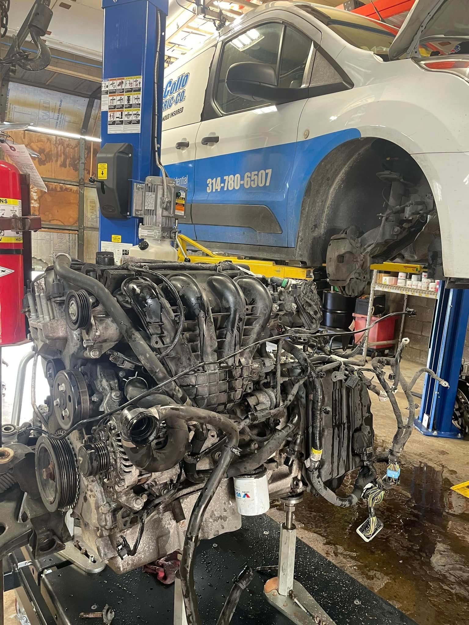 Charred engine assembly in an auto shop beside a silver car on a lift