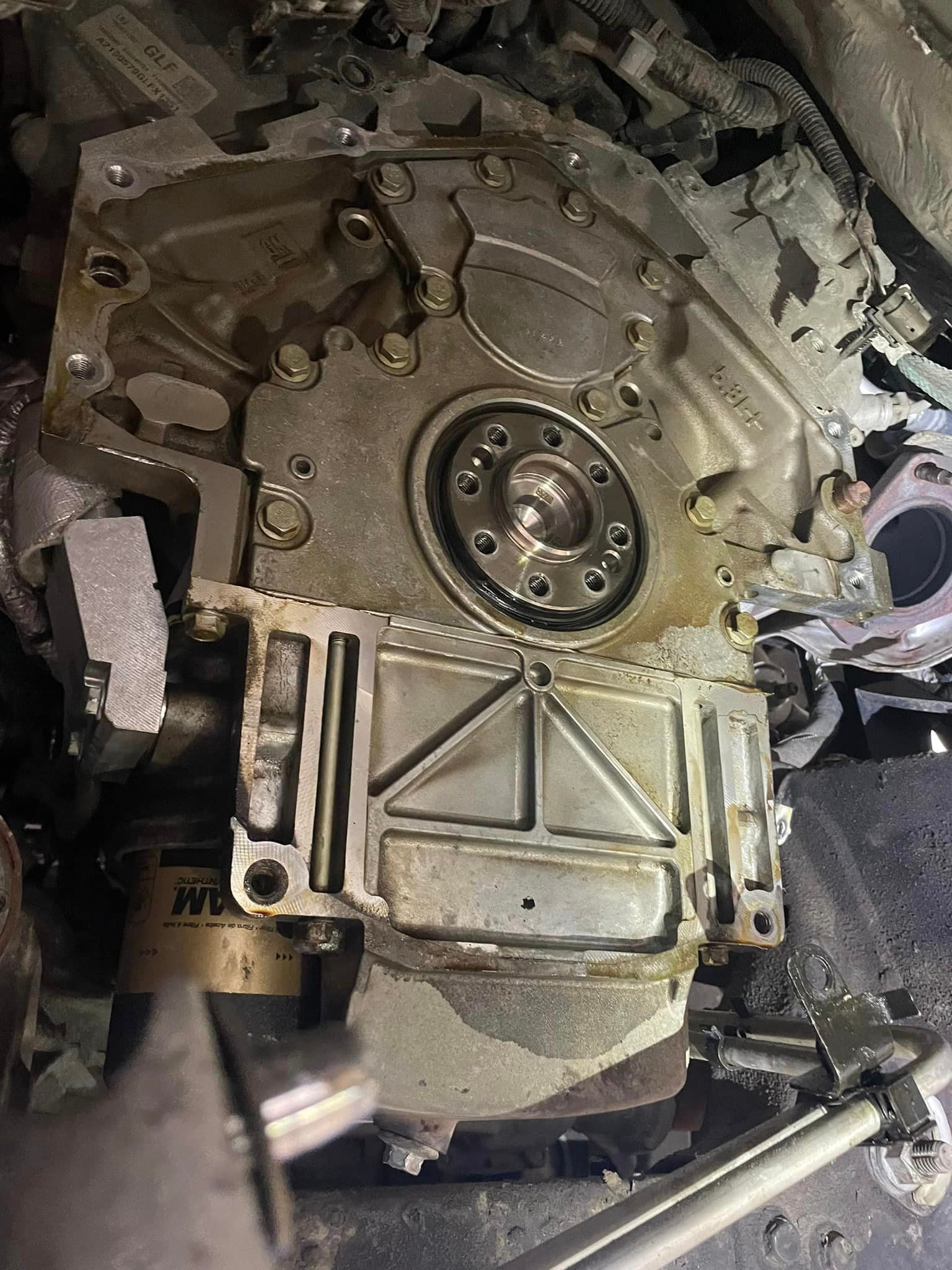 Close-up of a greasy mechanical engine or gearbox with bolts, hoses, and metal panels.