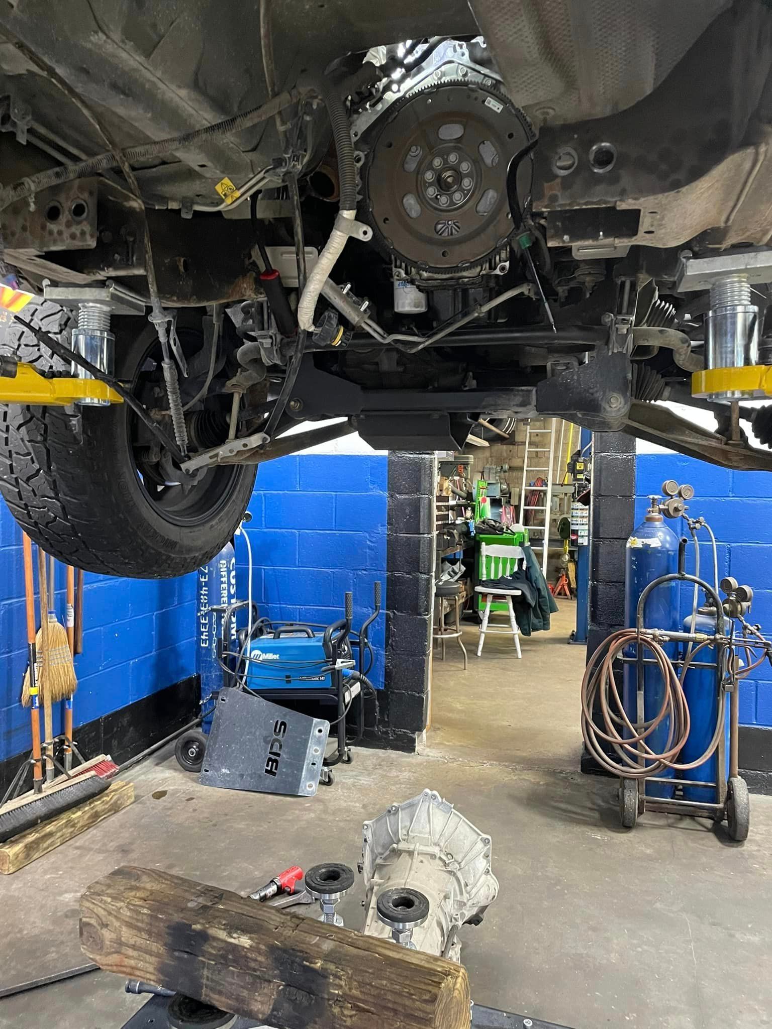 Undercarriage of a vehicle in a blue auto repair shop, with tools and equipment visible underneath.