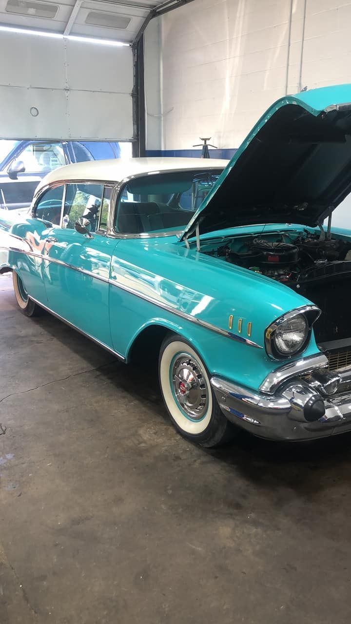 Turquoise classic car with hood open, parked indoors in a garage or workshop.