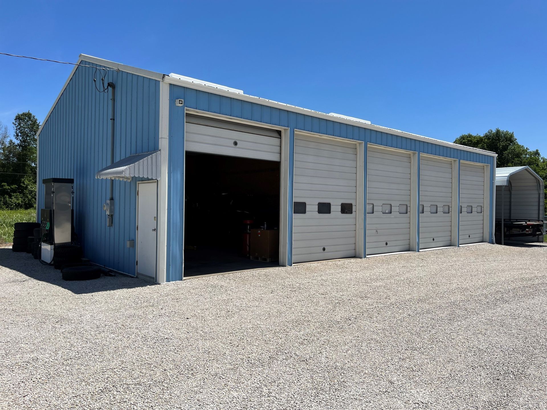 Blue metal storage building with open garage bays on a gravel lot under a clear sky