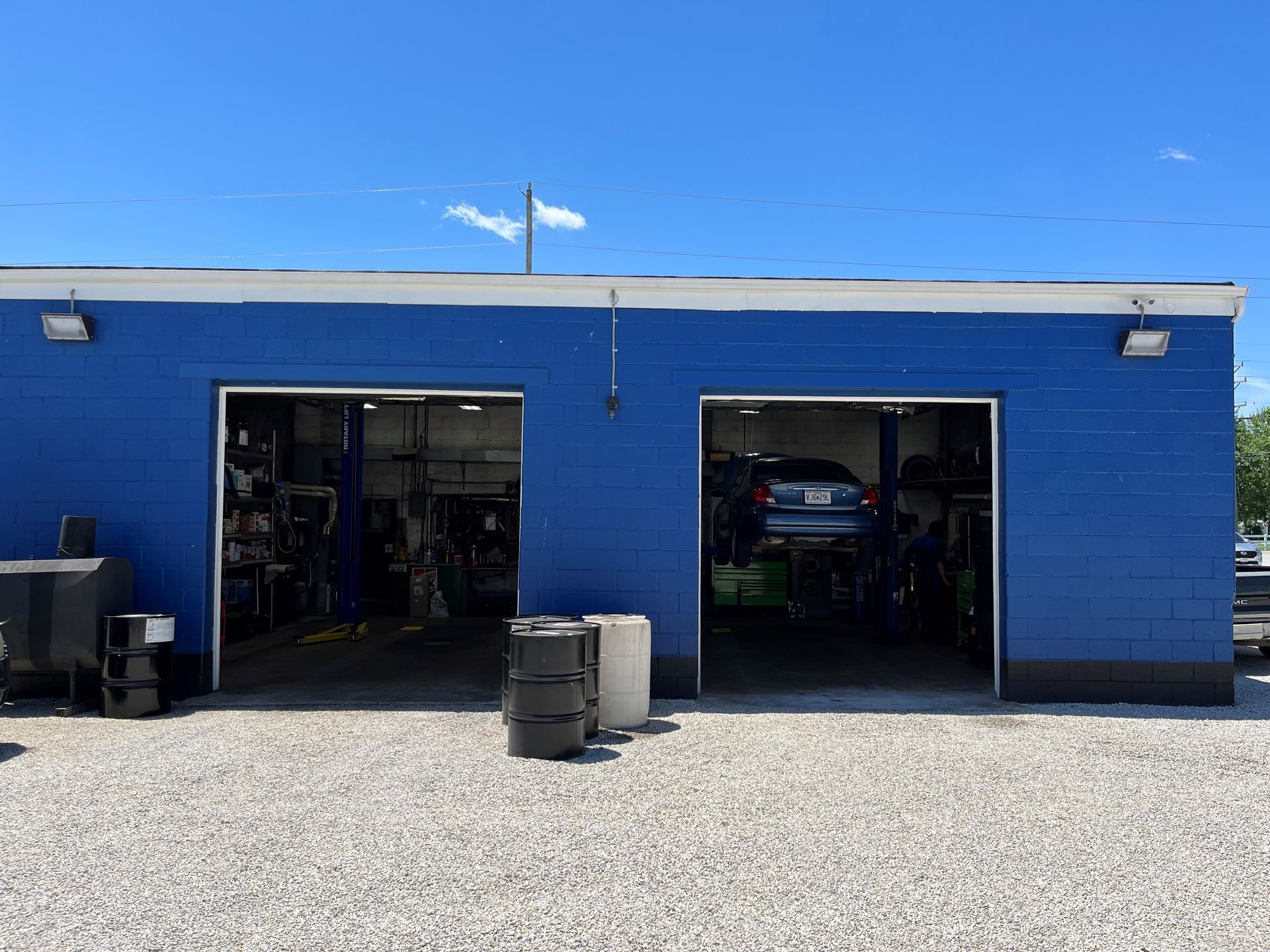Blue auto repair garage with two open bays and a gravel lot in front