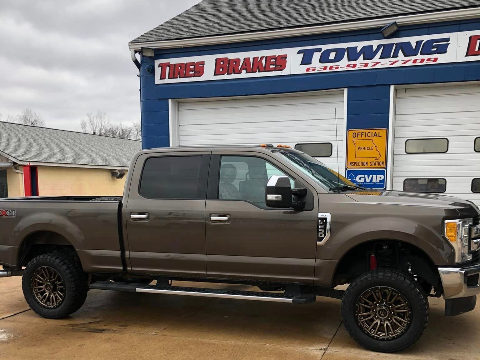 Brown pickup truck parked outside a tire and towing shop under a cloudy sky