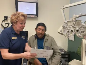 Optometrist assisting a patient with eye exam chart in an examination room.