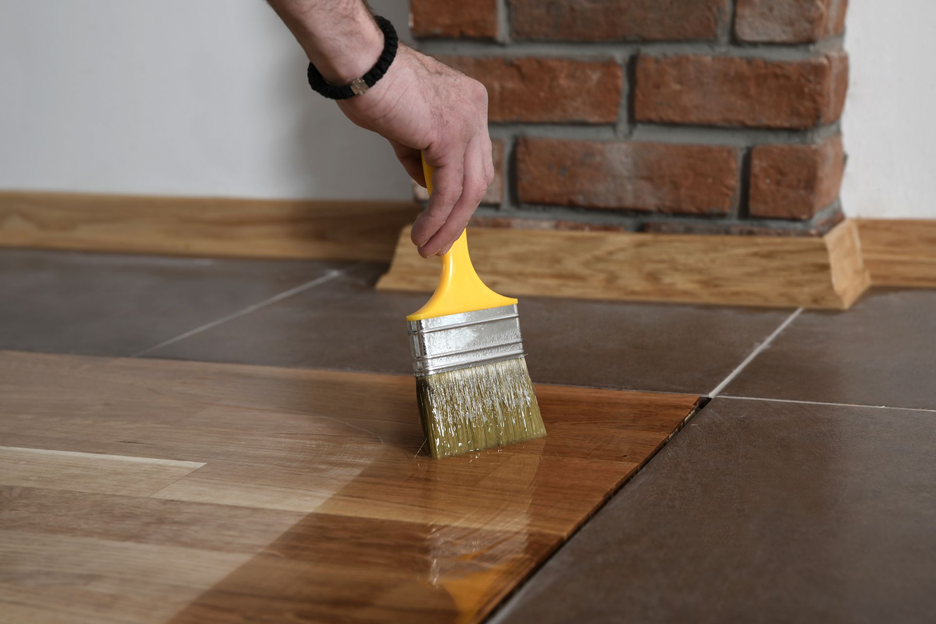 Person applying varnish to wooden floorboards with a paintbrush.