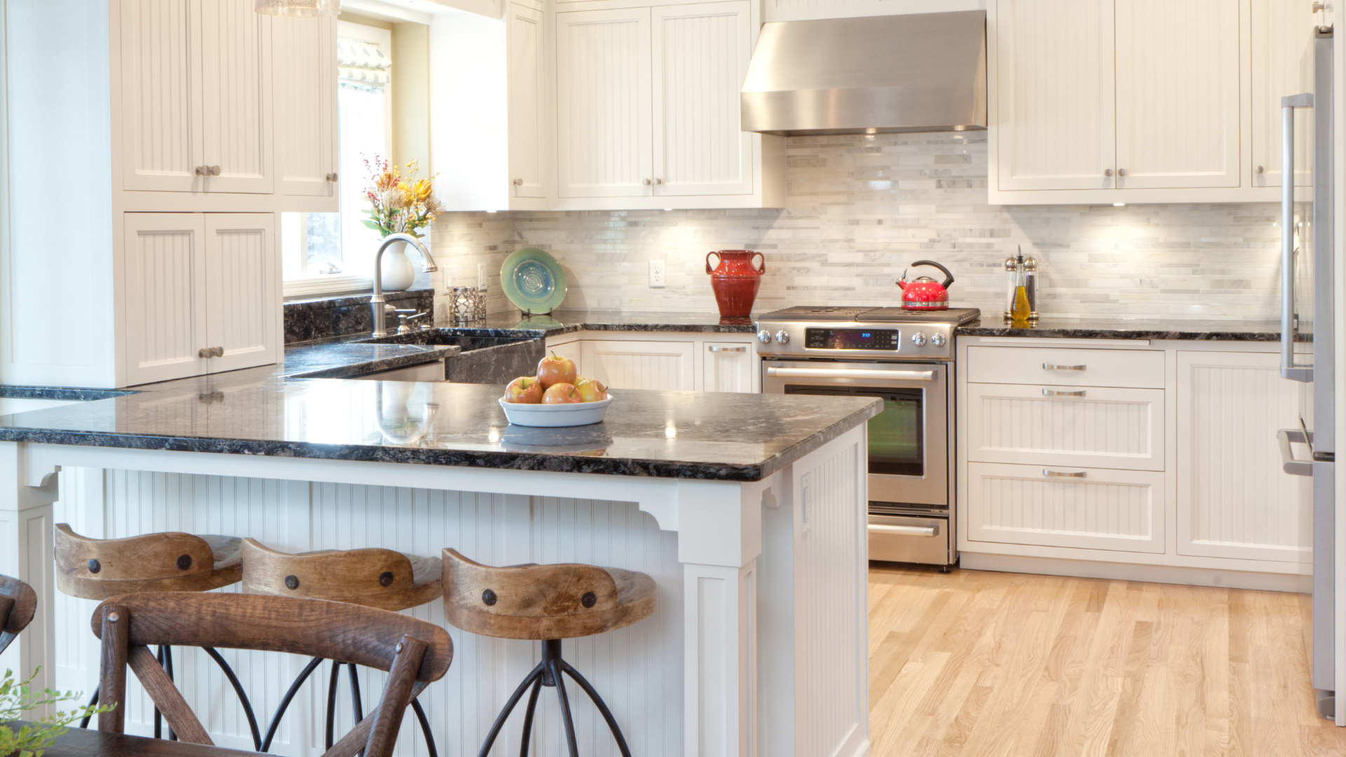 White kitchen with island, black granite countertop, stainless steel appliances, and wooden bar stools.