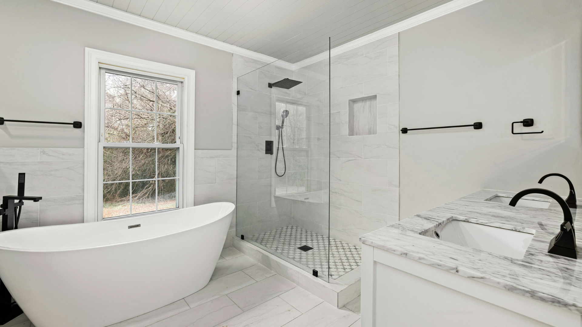 Elegant white bathroom with freestanding tub, glass shower, double sinks, and window.