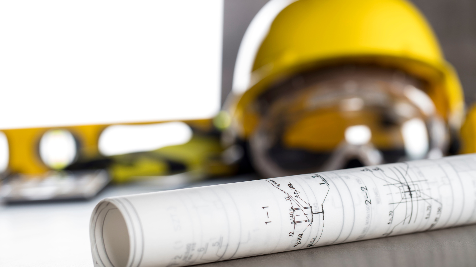 Rolled-up blueprint, yellow hard hat, safety glasses, and level; construction tools.