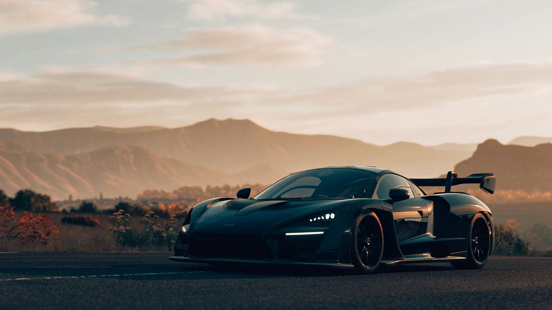 Black McLaren Senna on a road with mountains in the background, golden light, autumn setting.