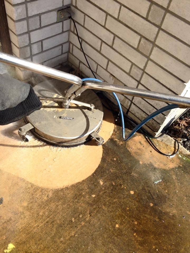 A machine is cleaning a dirty concrete floor in front of a brick building.