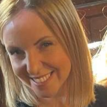 Woman with blonde hair, smiling, looking towards the camera.