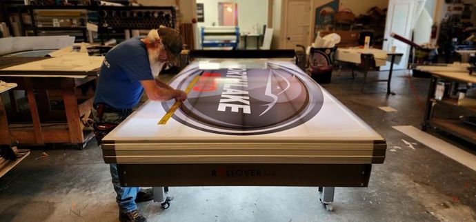 A man working on a large sign with a company logo in a workshop.