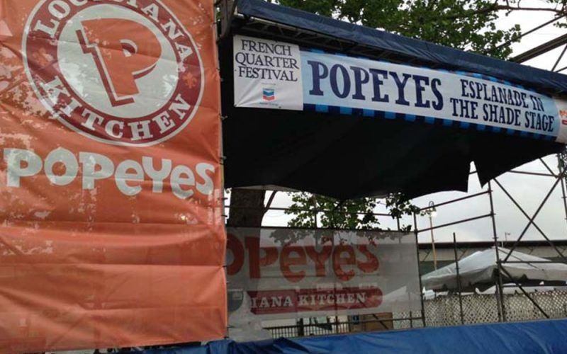 Popeyes booth at the French Quarter Festival. Orange and white signs with food and festival logos. 