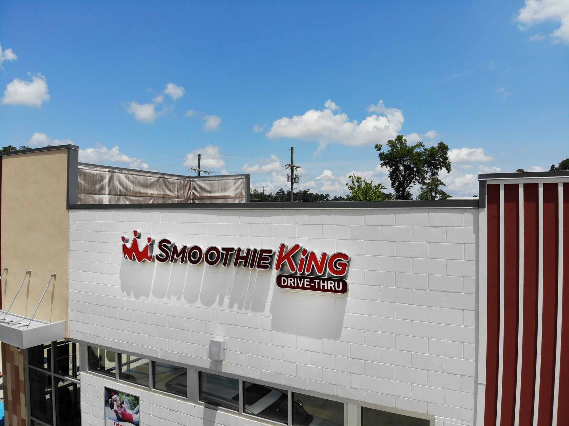 Smoothie King sign on a white brick building with drive-thru under a blue sky.