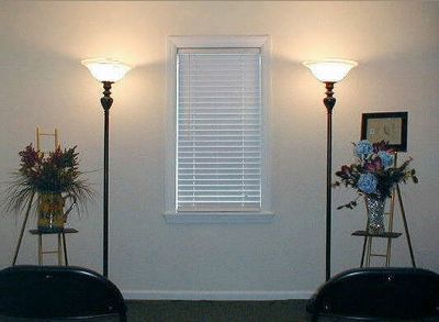Living room wall with centered window, two floor lamps, and floral arrangements on stands