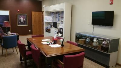 Conference room with wooden table, red chairs, wall-mounted TV, and display cabinets in a brown-walled office.