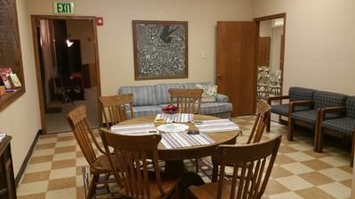 Lobby seating area with wooden chairs, round table, couch, and checkered tile floor near an exit sign
